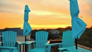 A deck with chairs and umbrellas, overlooking a residential area during sunset. - Walk to Beach, Jacuzzi, Treetop Deck, 4WD Pass, Love Pets! (Corolla)