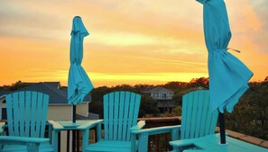 Eine Terrasse mit Stühlen und Sonnenschirmen, mit Blick auf eine Wohngegend bei Sonnenuntergang.