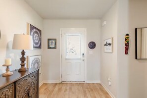 Ein Korridor mit einer weißen Tür, einem Holzschrank mit Lampe, gerahmten Bildern und einem Willkommensschild.