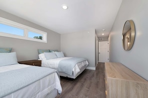 Une chambre avec deux lits, une commode en bois, un miroir et une fenêtre.