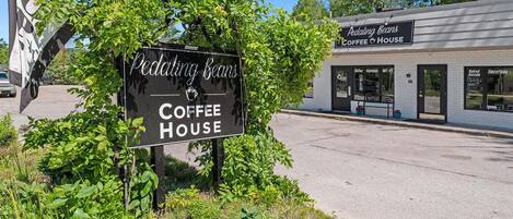A sign for Pedaling Beans Coffee House with a clear view of the building's entrance and a parking lot.