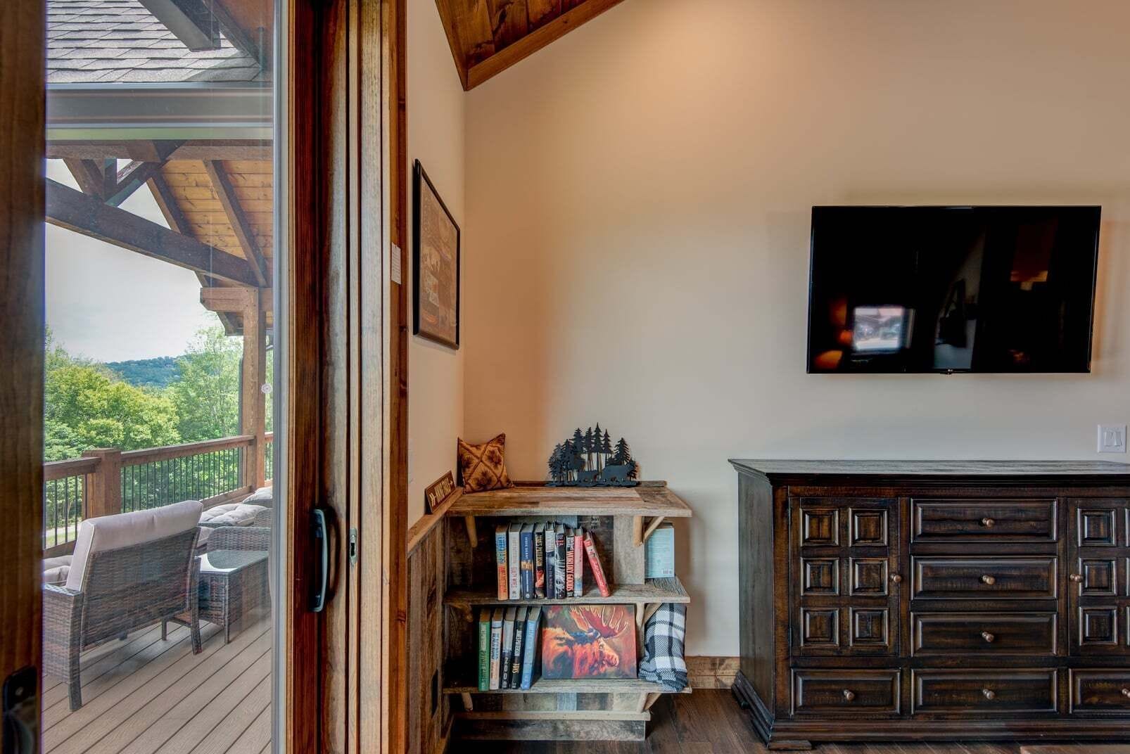 A room with a wooden deck, a bookshelf, a television, and a dark wooden cabinet.