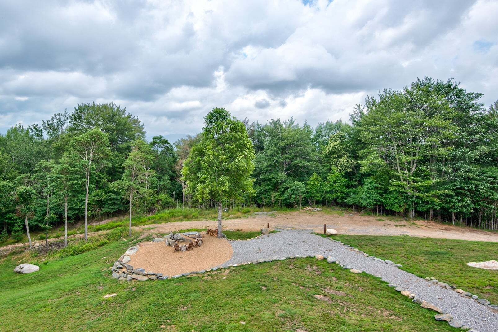 A natural outdoor area with a gravel path, a seating area, and trees.