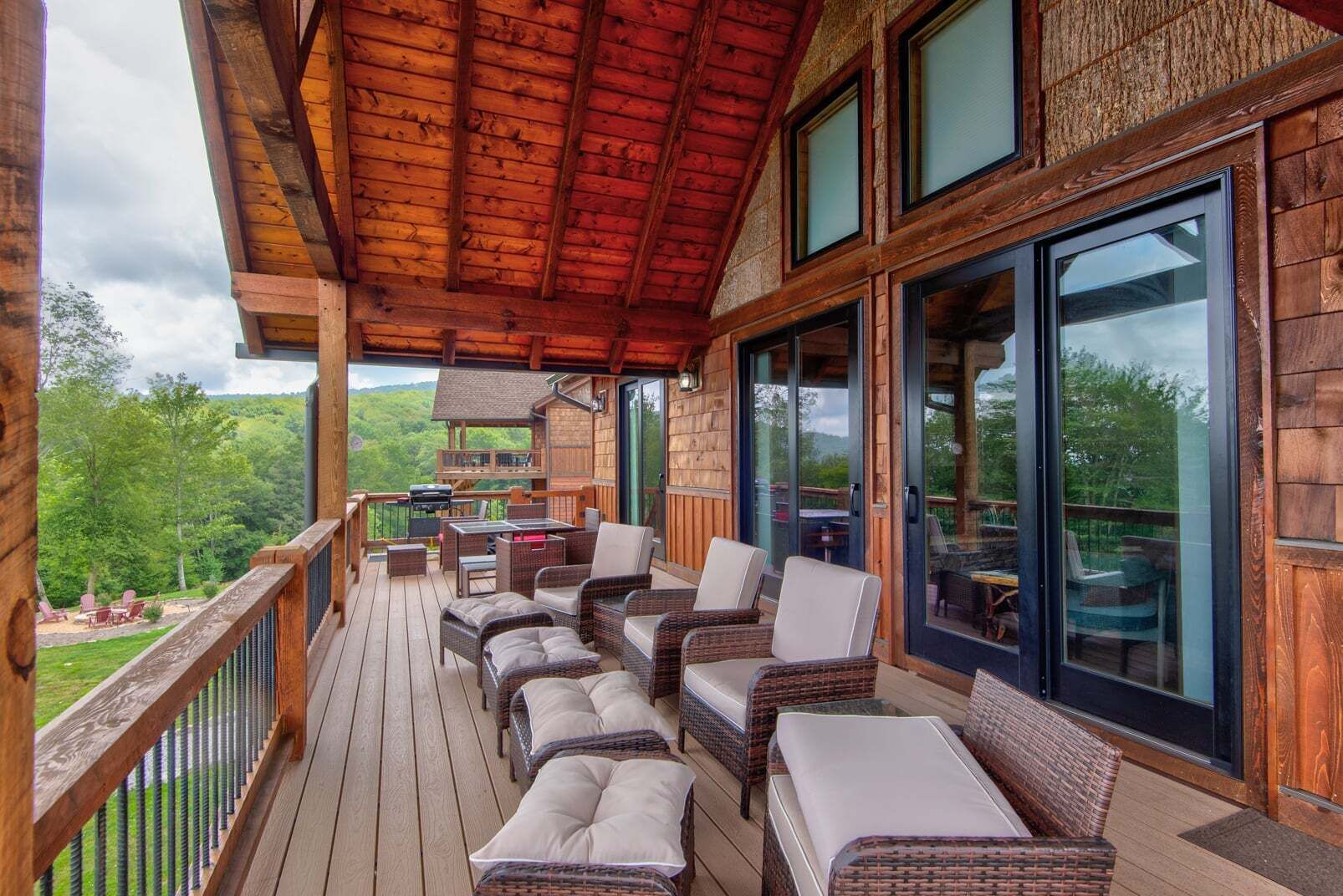 Una terraza de madera con muebles de mimbre, ventanas amplias y vistas al exterior.