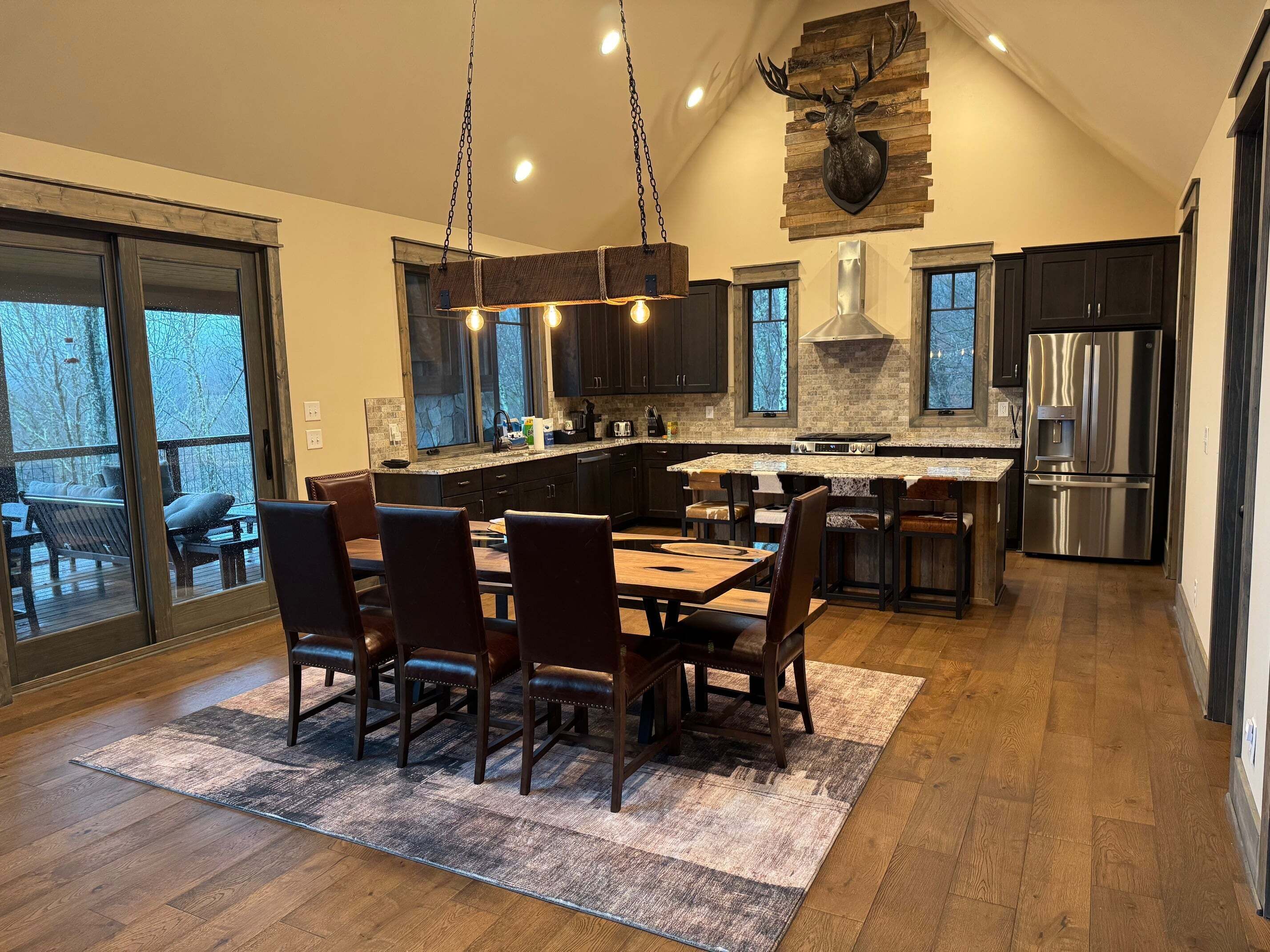 A modern kitchen with a large island, dark cabinetry, and a stone fireplace.