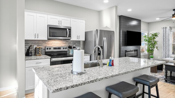 A modern kitchen with white cabinets, stainless steel appliances, a granite countertop, and a bar stool. - The Lookout (Clarksville)