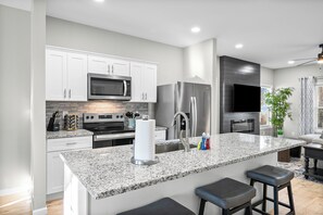 A modern kitchen with white cabinets, stainless steel appliances, a granite countertop, and a bar stool. - The Lookout (Clarksville)