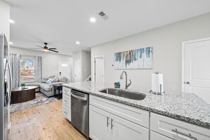 A modern kitchen with granite countertops, stainless steel appliances, and a dining area with a sofa and coffee table.