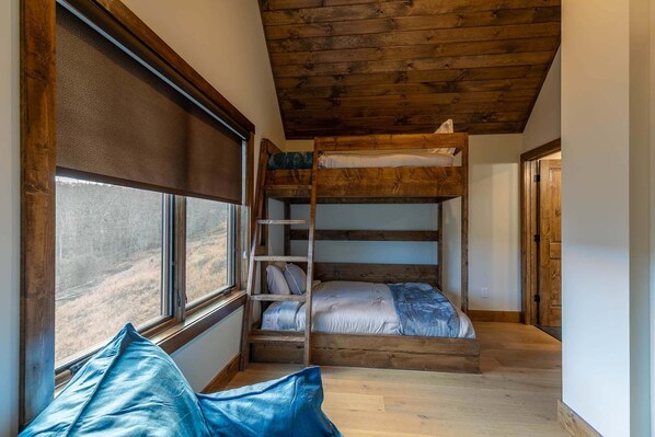 Dormitorio con literas, ventana, techo de madera y escalera.