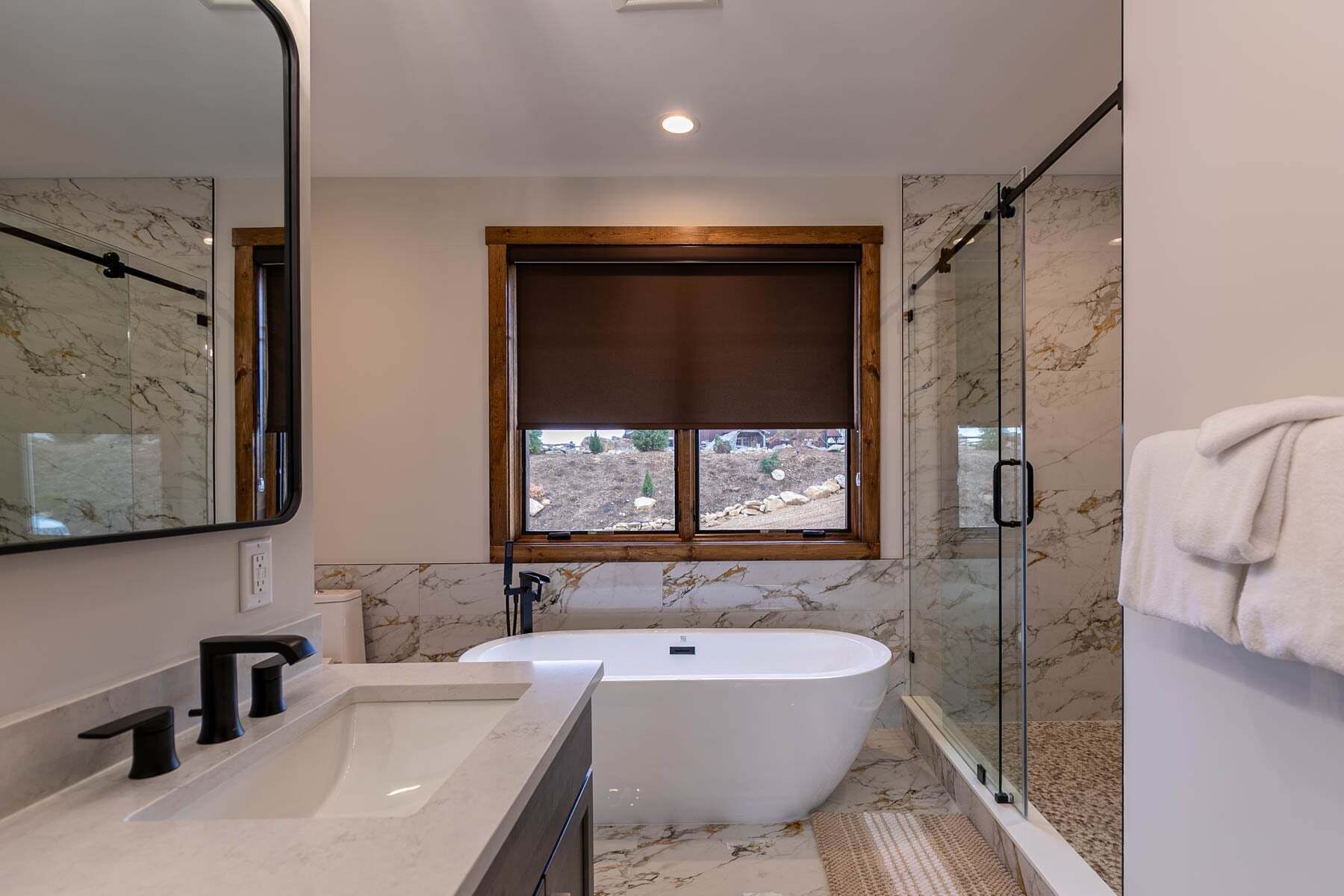 Un baño moderno con una bañera independiente, un espejo grande y una ventana con vistas al exterior.