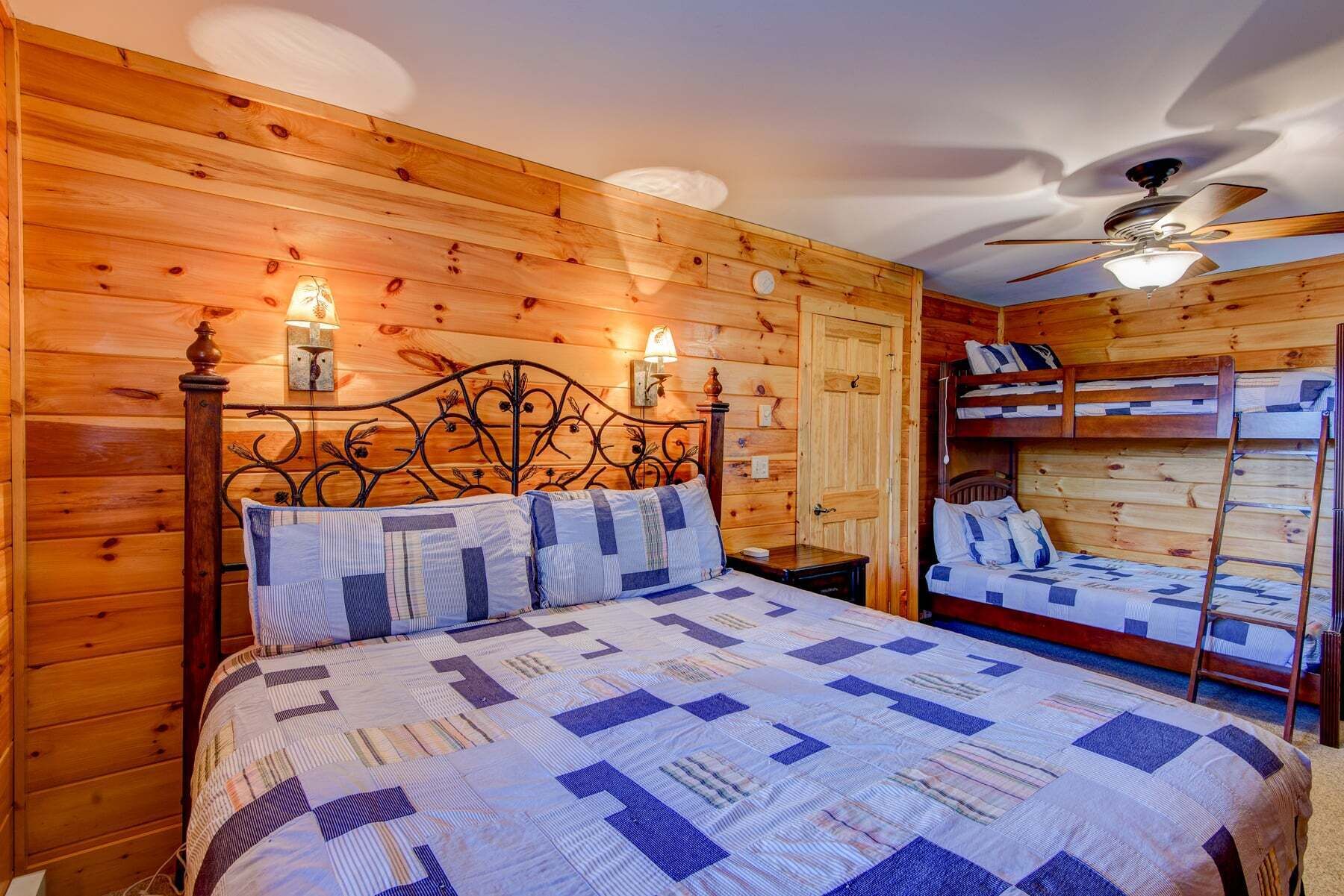 Ein Schlafzimmer einer Holzhütte mit einem Bett, einem Nachttisch, einem Deckenventilator und einem Etagenbett.