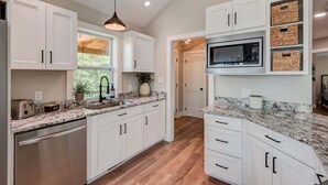 A modern kitchen with white cabinets, granite countertops, a stainless steel dishwasher, a microwave, and a hanging pendant light. - Lessons From Mars (Banner Elk)