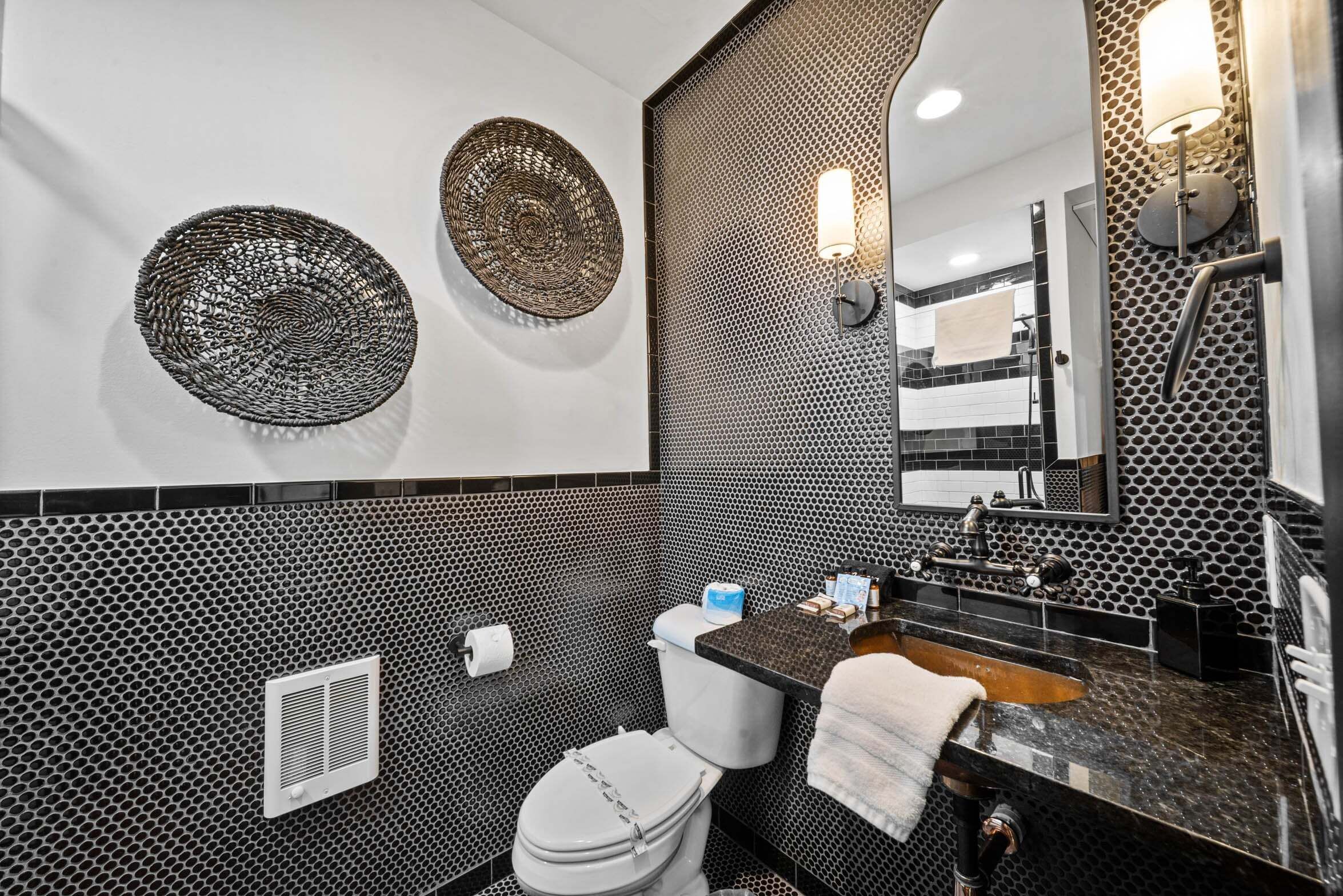 Une salle de bain moderne avec un mur recouvert de carreaux noirs et blancs, des toilettes, un lavabo avec une serviette et des éléments décoratifs muraux.
