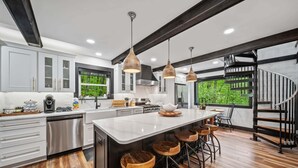 A modern kitchen with a central island, bar stools, stainless steel appliances, and a spiral staircase. - The Beech House (Banner Elk)