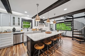 Una cocina moderna con una isla central, taburetes de bar, electrodomésticos de acero inoxidable y una escalera de caracol.