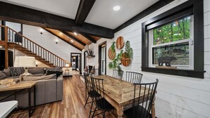 A modern interior with a wooden dining table, black chairs, a gray sofa, and a staircase. - The Beech House (Banner Elk)