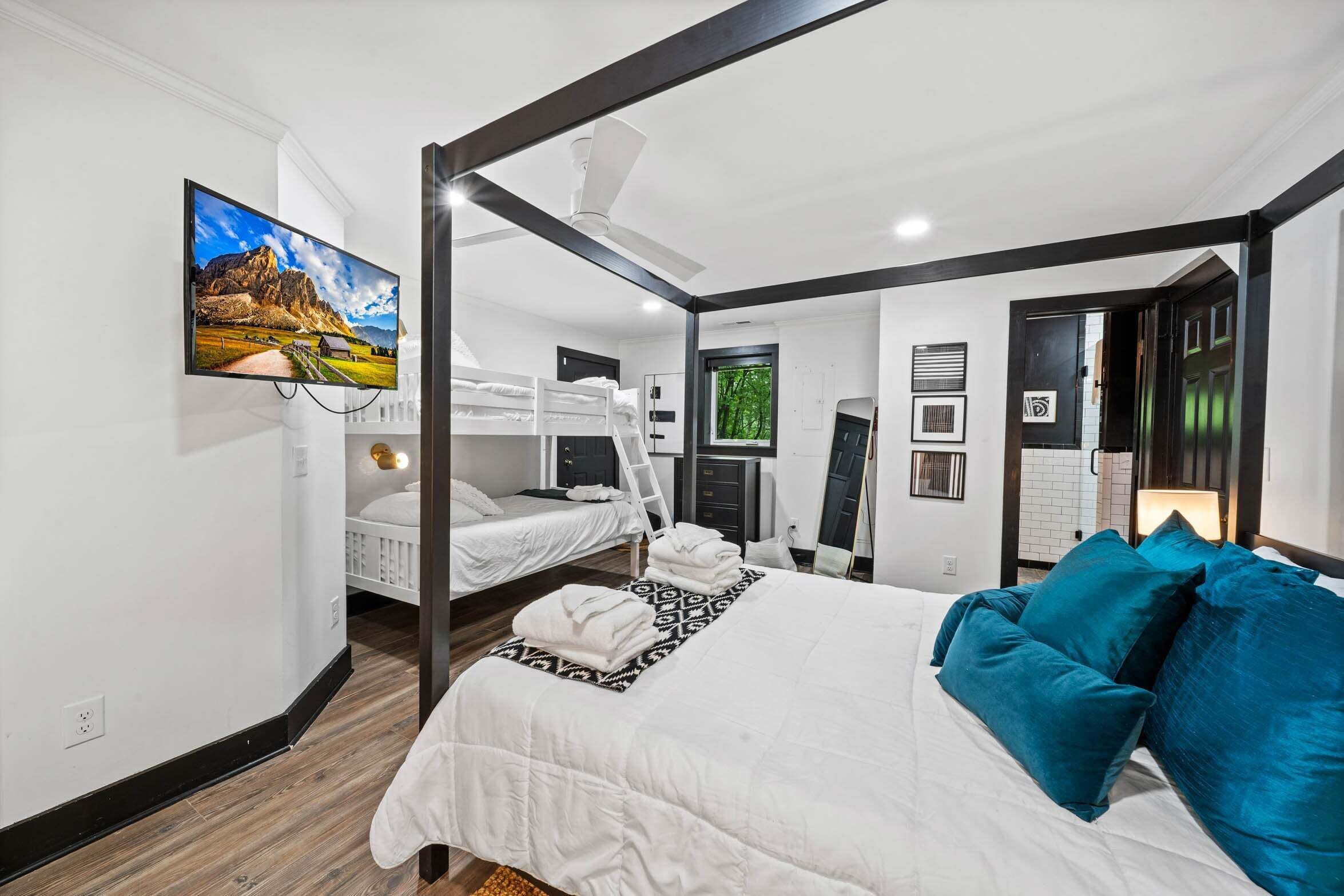 Une chambre d’hôtel moderne dotée d’un grand lit, de deux petits lits, d’un ventilateur de plafond, d’une télévision et d’une fenêtre offrant une vue agréable.