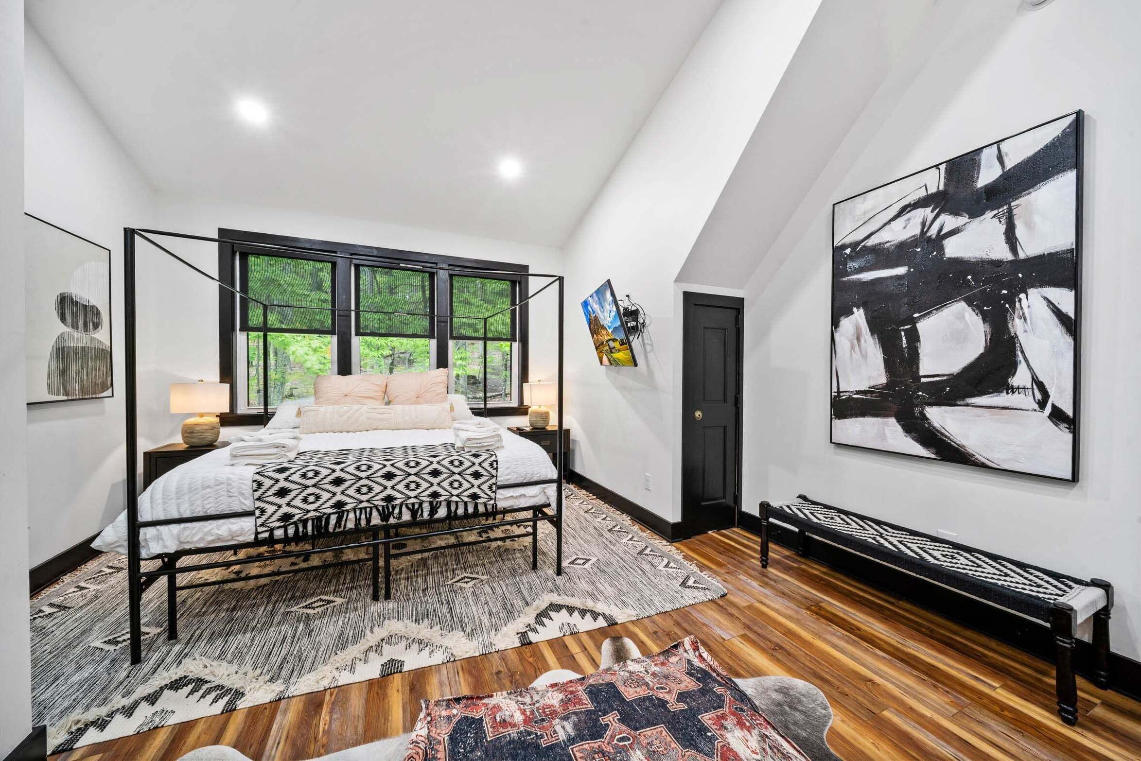 A bedroom with a bed, a window, a painting, and a bench.