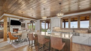 A spacious kitchen with a large island, bar stools, a fireplace, and a stone backsplash. - Amongst the Clouds at Chappell Farms (Banner Elk)