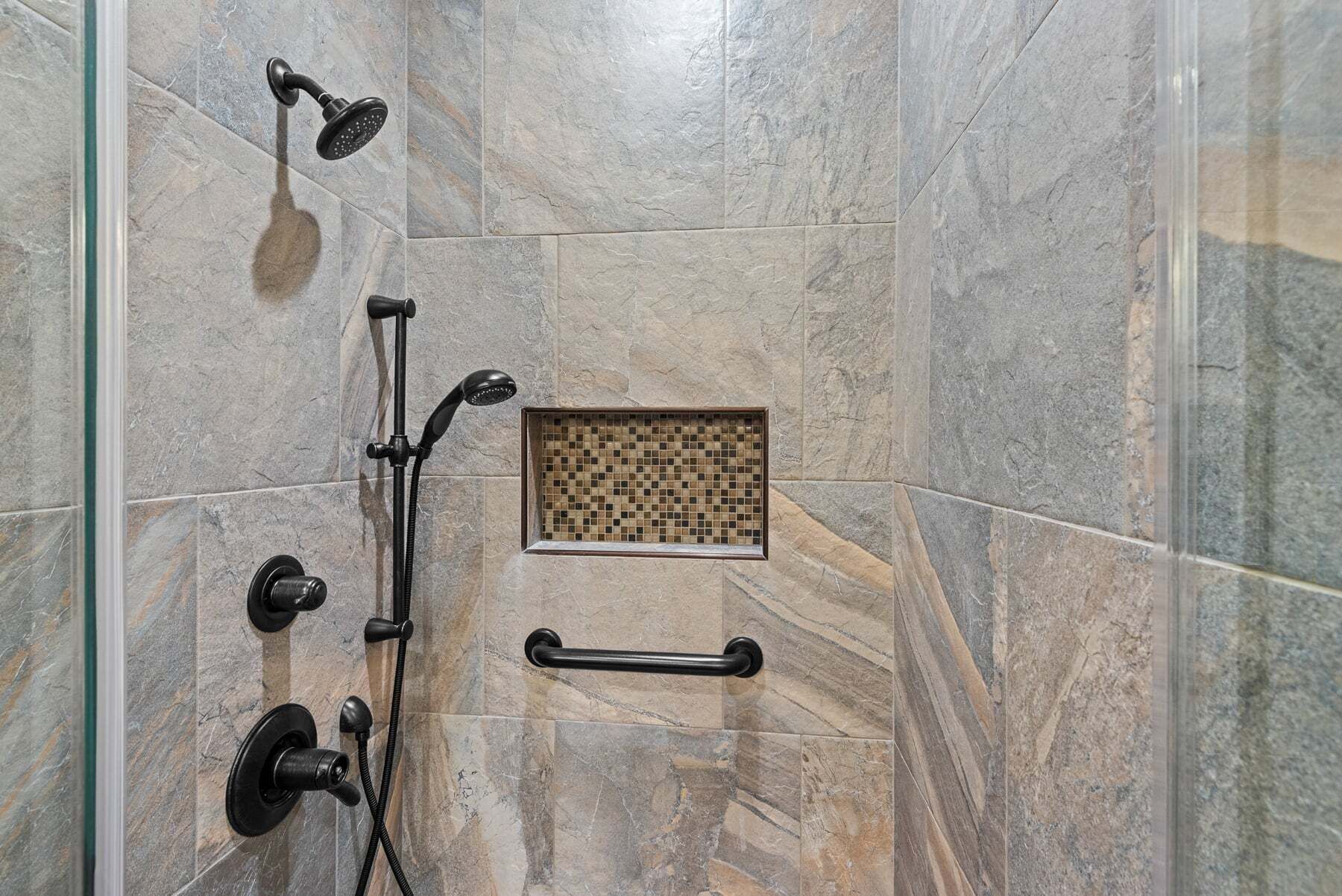 A shower with a handheld showerhead, a wall-mounted showerhead, and a handheld shower attachment.