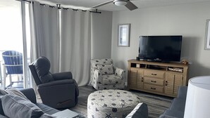Ein Wohnzimmer mit Sofa, Hocker, Sessel, Fernseher, Holzschrank und Deckenventilator.