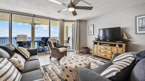 Ein Wohnzimmer mit großem Fernseher, bequemen Sitzgelegenheiten, Deckenventilator und Meerblick.