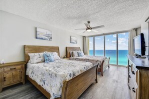 Ein Schlafzimmer mit zwei Betten, einem Deckenventilator, Kunstwerken, einem Fernseher und Blick aufs Meer.