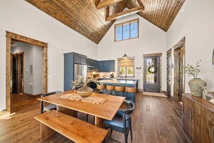 Una cocina amplia con vigas de madera, una isla central y una zona de comedor con una mesa y bancos de madera.