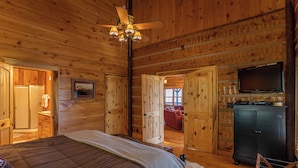 Ein Schlafzimmer einer Holzhütte mit einem Bett, einem Deckenventilator, einem Fernseher und einem Schrank.