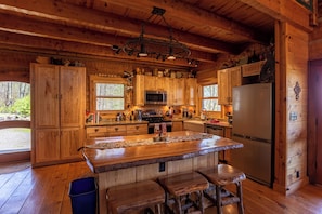 A wooden cabin kitchen with a central island, bar stools, a refrigerator, and wooden cabinets. - Van Beek's Peak (Banner Elk)