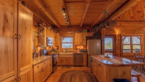 Ein Interieur einer Holzhütte mit Küche, Holzschränken, einem Essbereich und einem großen Fenster.