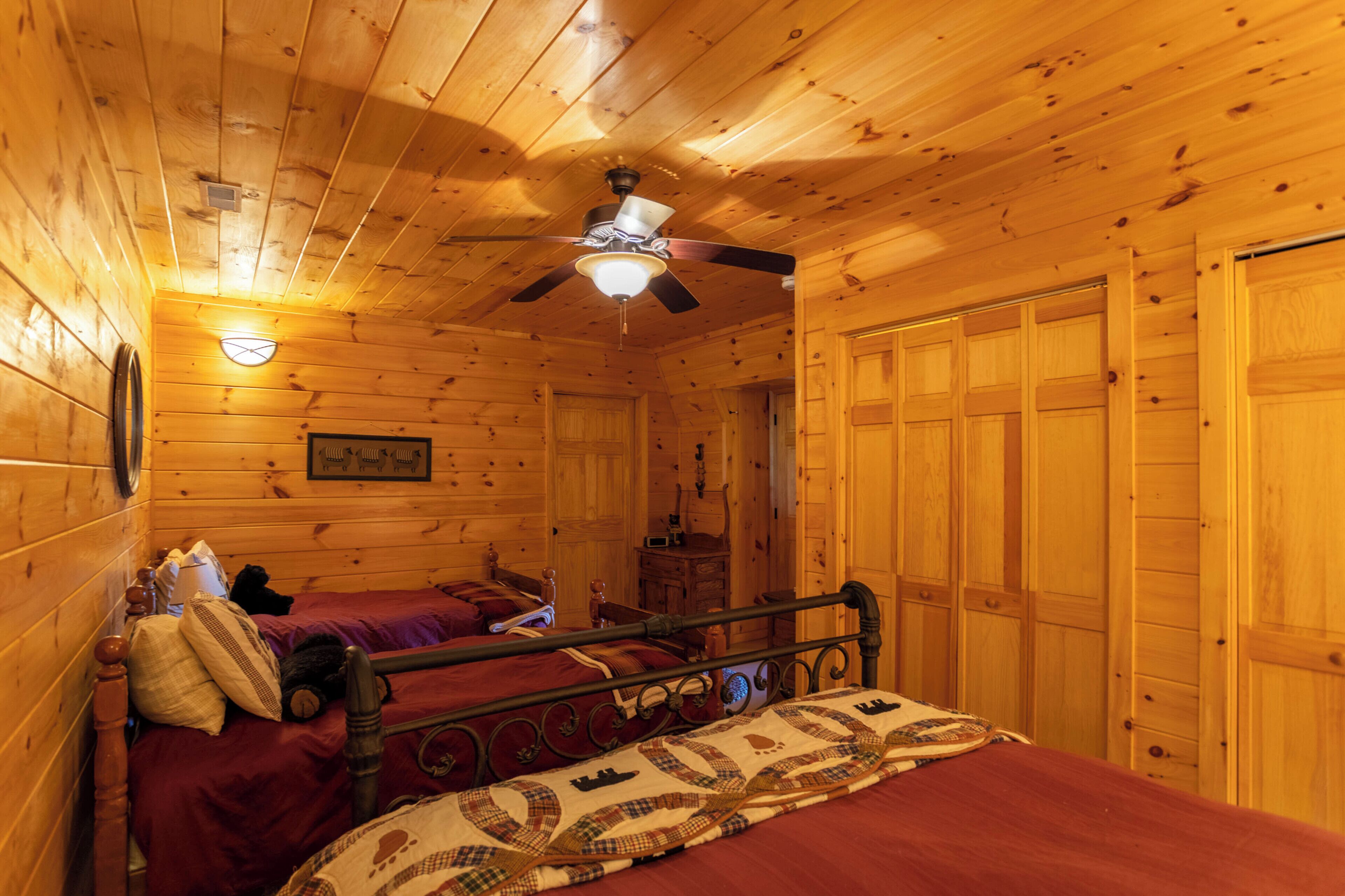 Een houten kamer met slaapkamer met twee bedden, een plafondventilator en houten wanden.