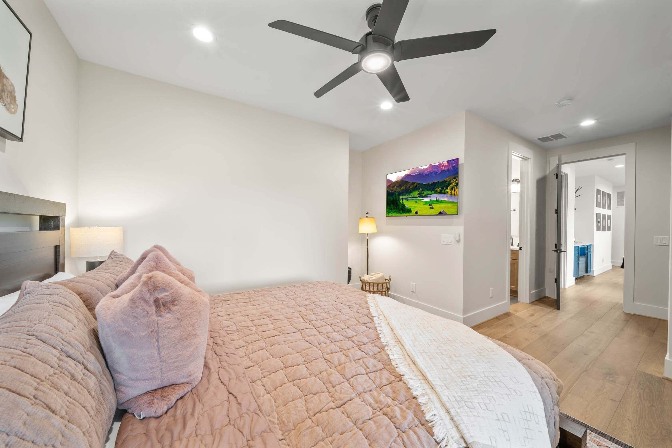A bedroom with a bed, a ceiling fan, a nightstand, a lamp, and a painting on the wall.