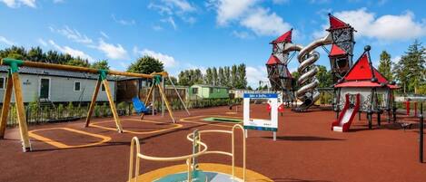 A playground with various play structures, including swings and climbing frames, under a clear blue sky.