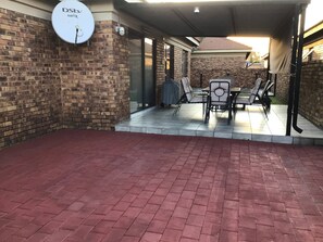 Eine Pflasterterrasse mit überdachter Sitzgruppe, einer Satellitenschüssel und einer Überwachungskamera.