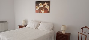 A bedroom with a bed, two bedside tables, a radiator, and a painting on the wall.