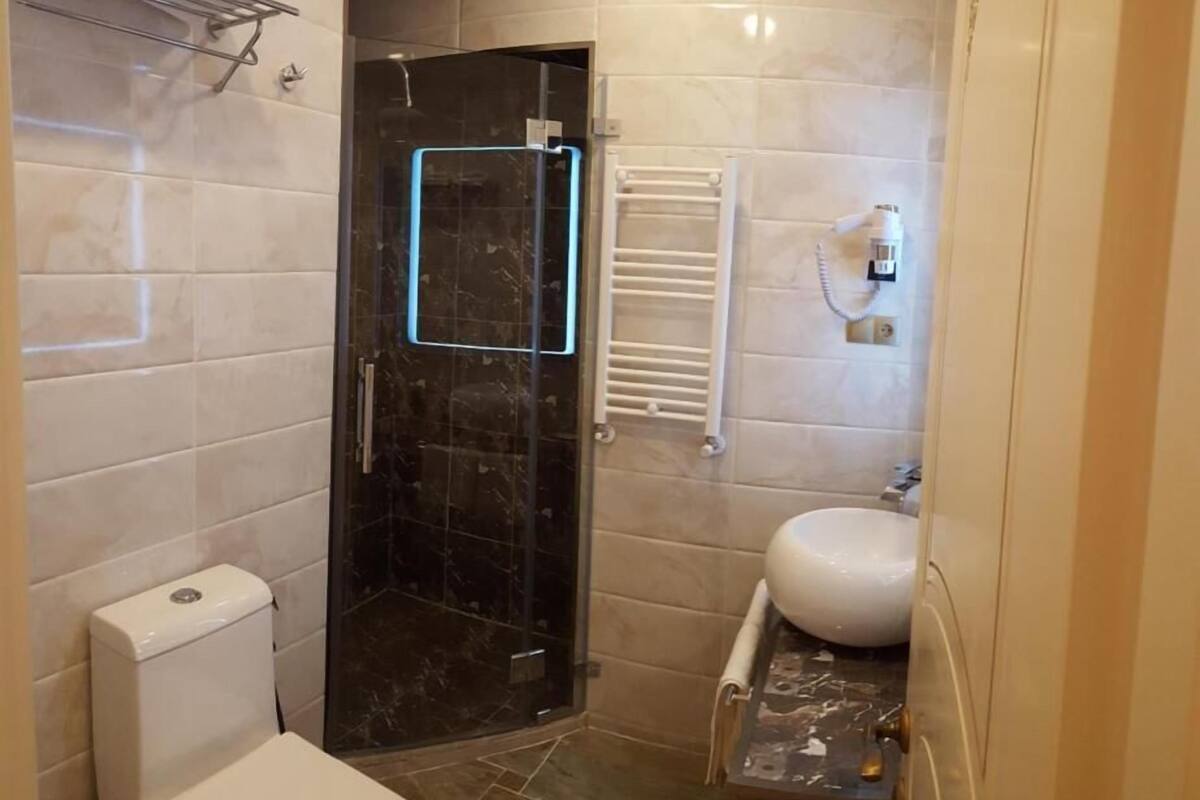 Un baño con inodoro, lavamanos, toallero y ducha con puerta de cristal.