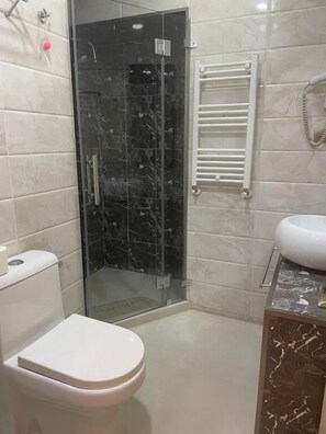 A bathroom with a toilet, a glass-enclosed shower, and a sink with a marble countertop. - X Seven plus Tbilisi (Tbilisi)