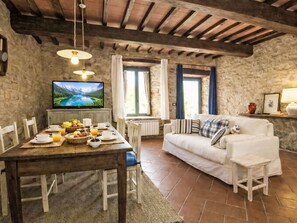 A rustic room with stone walls, a wooden dining table set with breakfast, a white sofa, and a television displaying a mountainous landscape. - Le Mangiatoie by Interhome (Rufina)
