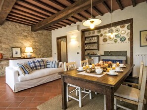 A rustic dining area with a wooden table set for breakfast, a white sofa with plaid cushions, and a stone wall. - Le Mangiatoie by Interhome (Rufina)