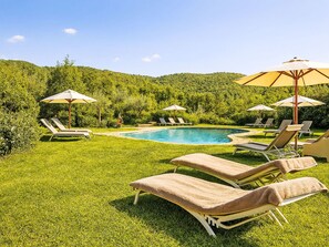 A pool area with lounge chairs and umbrellas, surrounded by lush greenery and hills. - Il Guscio by Interhome (Rufina)
