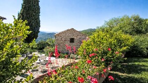 A stone building with a garden patio, surrounded by greenery and hills in the background. - Il Guscio by Interhome (Rufina)
