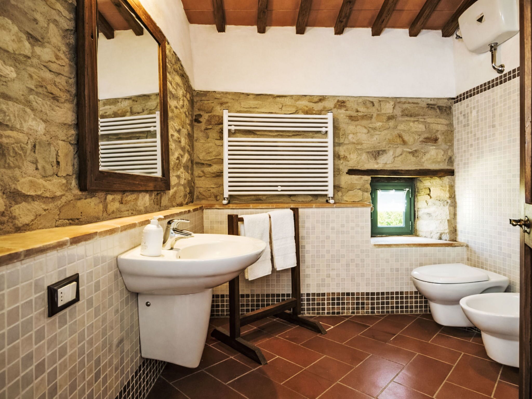 Une salle de bain avec un mur en pierre, un lavabo, des toilettes et une fenêtre.