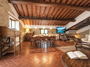 A rustic dining area with a wooden table and chairs, a stone wall, and a television on the wall. - La Noce by Interhome (Rufina)