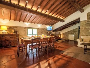 A dining area with a wooden table and chairs, a stone wall, and a television mounted on the wall. - La Noce by Interhome (Rufina)