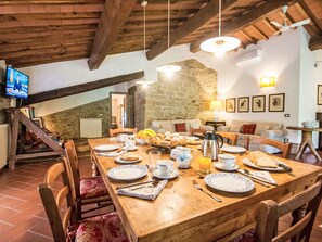 A dining area with a wooden table set for breakfast, stone walls, and a television in the background. - in Toscana La noce di Francesca by Interhome (Rufina)
