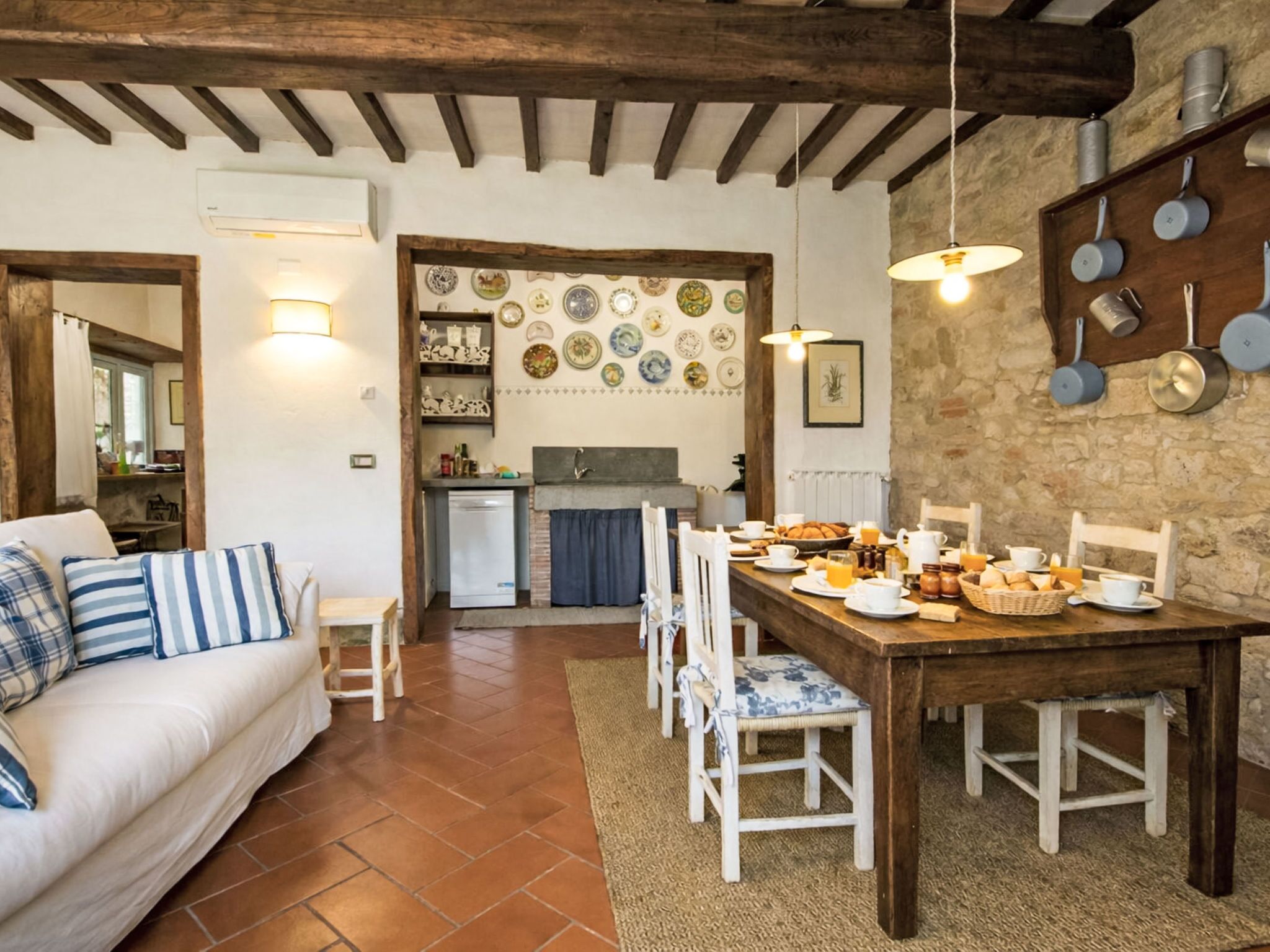 Un salón acogedor con un sofá, una mesa de comedor y sillas. Se observa una zona de cocina con un refrigerador, fregadero y diversos utensilios.
