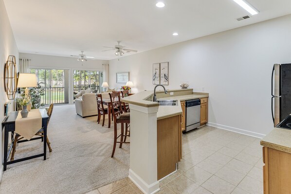 A modern kitchen with a central island, a dining area with chairs and a table, and a view of the outdoors through large windows.