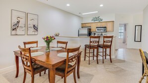 A dining area with a wooden table and chairs, a vase with flowers, and a kitchen in the background. - Condo in Sea Trail, GREAT GOLF view, Restaurants on site, pool at the complex.  (Sunset Beach)