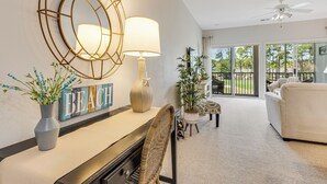 A living room with a fireplace, a wall-mounted mirror, a lamp, a wicker chair, and a couch. - Condo in Sea Trail, GREAT GOLF view, Restaurants on site, pool at the complex.  (Sunset Beach)